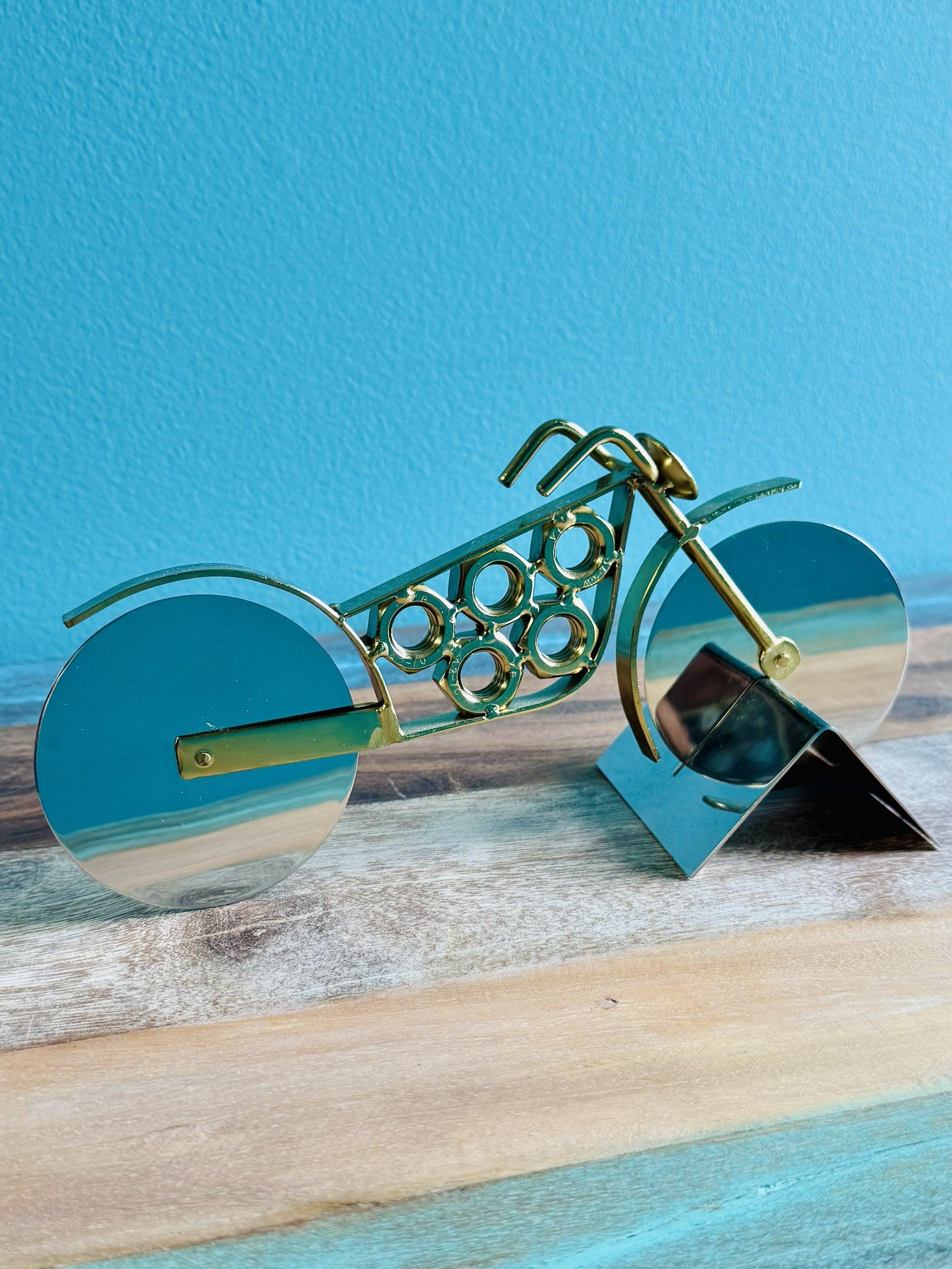 Gold motorcycle pizza cutter with stainless steel wheel blades on a teal stand
